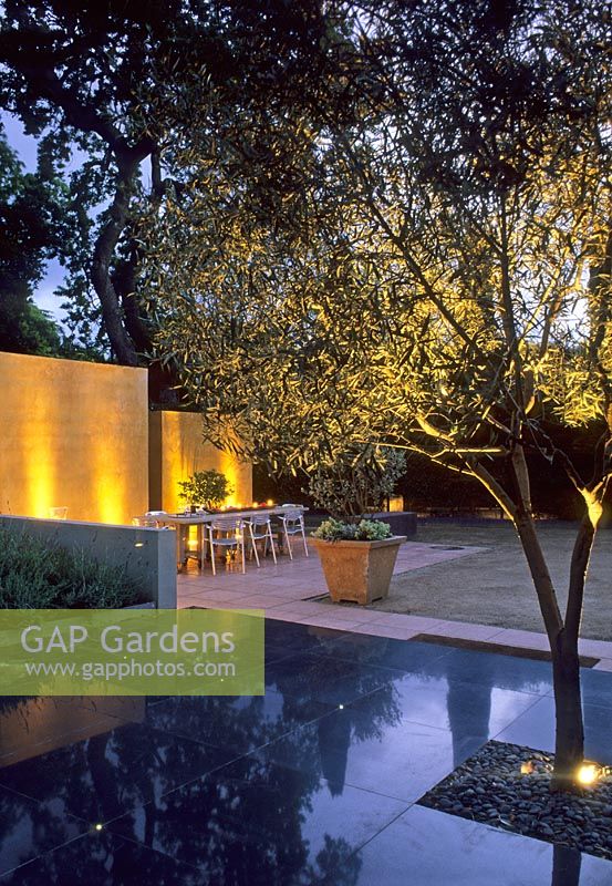 Jardin moderne avec dallage en pierre noire, arbre et coin repas éclairé le soir - Californie, USA