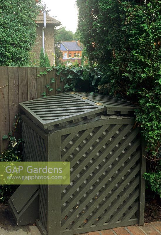Joli bac à compost en bois peint en vert dans un coin de jardin par une clôture dans le jardin de Londres
