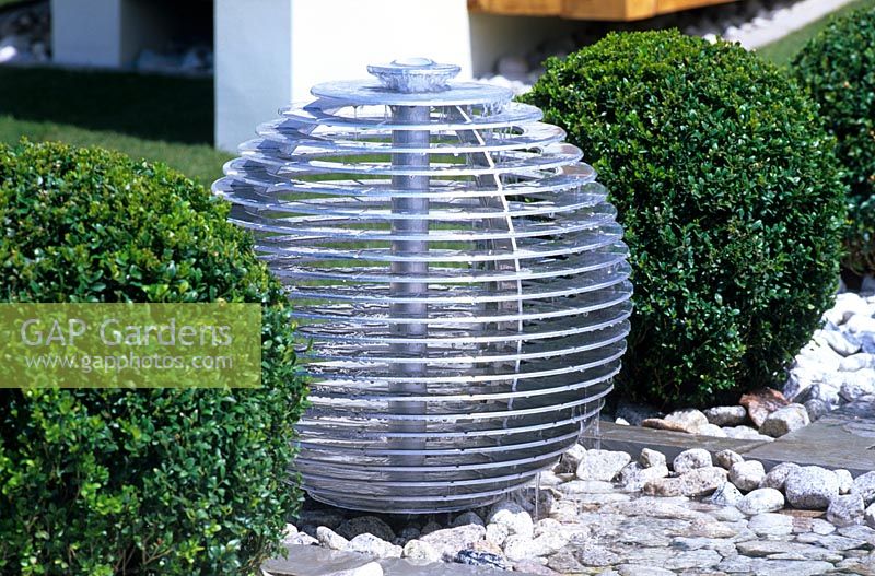 Une pièce d'eau sphérique avec des boules de topiaire Buxus coupé dans le jardin 'The Winalot Live a Lot' conçu par Chris Beardshaw au RHS Hampton Court Flower Show