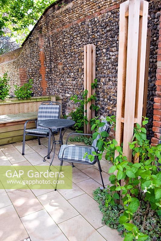 Petite terrasse avec dallage en pierre calcaire et piliers en teck dans un petit jardin moderne.