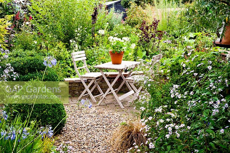 Table et chaises peintes avec pot de géraniums blancs sur une petite terrasse en brique - Brook Hall Cottages, Essex NGS