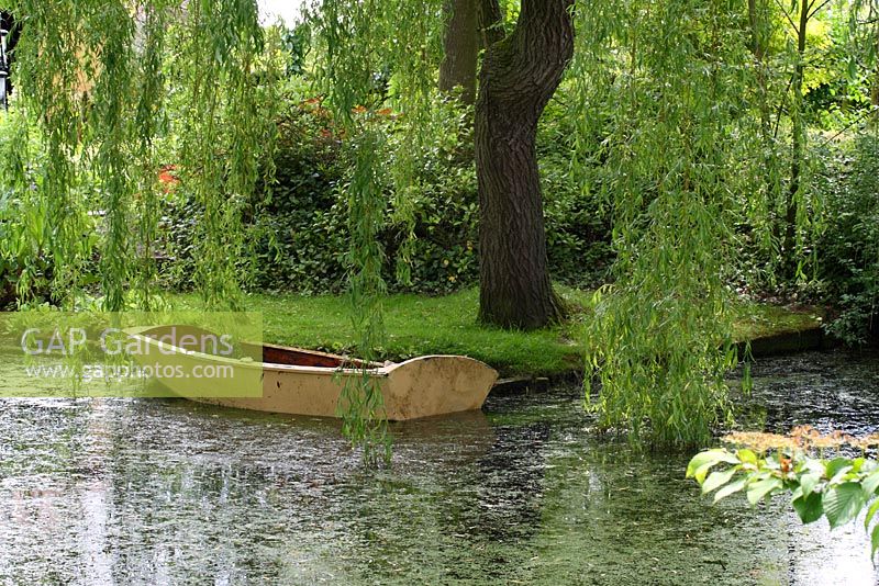 Vieux bateau à rames en bois dans l'étang ombragé par un saule pleureur - Sallowfield Cottage B