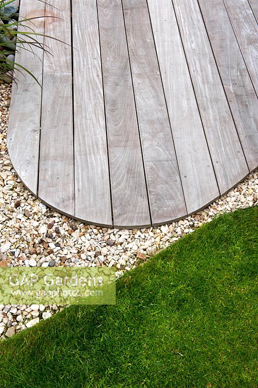 Le bord sinueux incurvé du platelage en bois dur Ipe contraste avec la courbe de la pelouse avec une bordure métallique nette et 20 ml de gravier