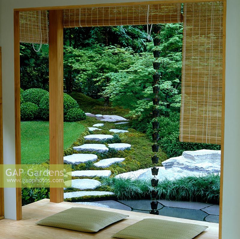 Vu de la véranda, le paysage japonais naturel idéalisé d'un ruisseau sec, une piscine peu profonde alimentée par une chaîne de pluie depuis le toit, les rochers, le chemin de pierre et le bois.