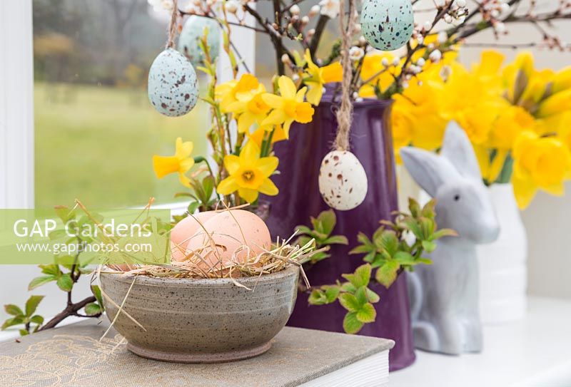 Affichage floral contenant des œufs décoratifs, des jonquilles, un feuillage printanier en fleurs et un lapin, en vue du jardin