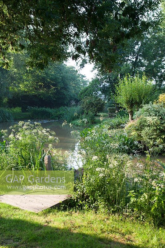 Jetée en bois le long d'un lac paysager dans un jardin de campagne mature en été. Galerie Bradness, East Sussex. Propriétaires: Artistes Michael Cruickshank et Emma Burnett