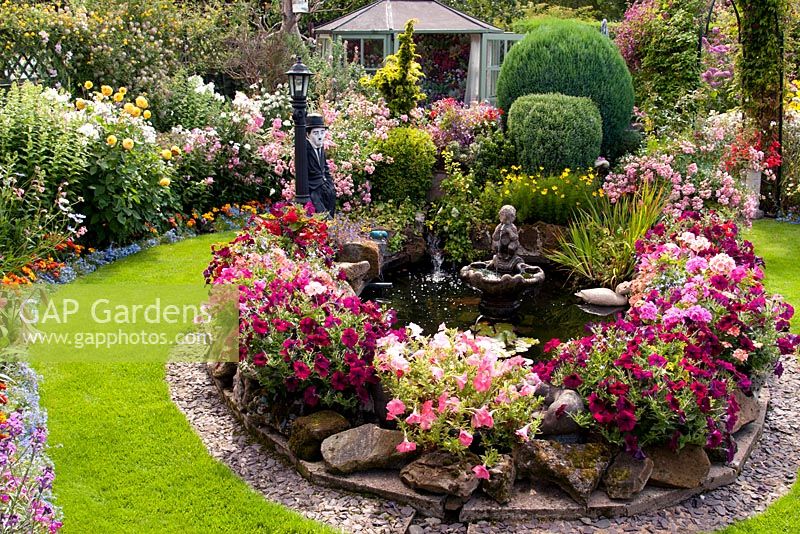 Jardin arrière coloré avec étang et rocailles mélangées remplies de plantes annuelles, d'arbustes et de vivaces. Pavillon d'été et pelouse. Manvers Street, DGS Derbyshire, août