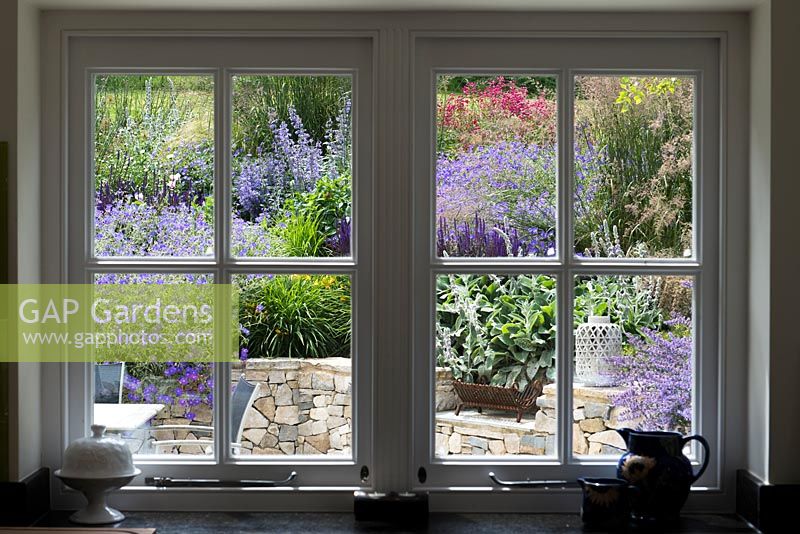 Une vue de la véranda d'une terrasse et d'un coin salon planté de vivaces et de graminées ornementales.