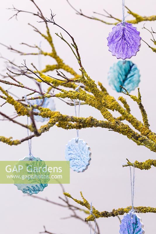 Décorations en argile peinte avec des empreintes de feuillage de pin, suspendues à une branche recouverte de lichen
