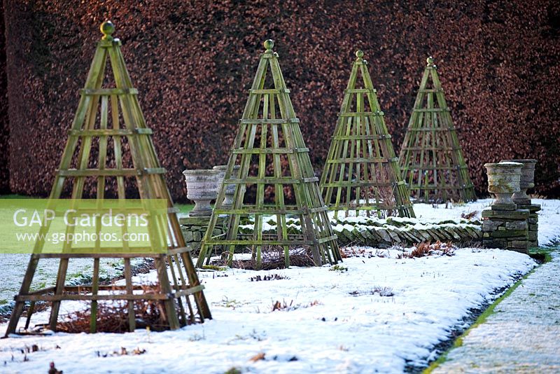 Parterres herbeux recouverts de neige avec des obélisques pyramides en bois à Levens Hall and Garden, Cumbria, Royaume-Uni.