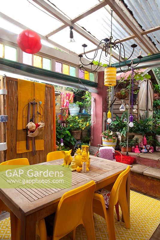 Le jardin du centre-ville avec des bégonias et des spathiphyllums présente des pièces rétro éclectiques colorées provenant des marchés locaux, y compris une salle à manger en bois avec des chaises jaunes