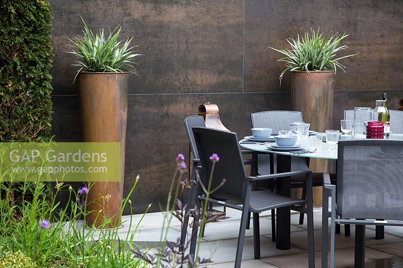 Jardin de banlieue contemporain avec mur en cuivre, pots et coin salon