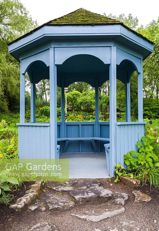 Gazebo en bois peint en bleu avec des bancs intégrés et des bardeaux de cèdre recouverts de Bryophyta verte - Mousse surplombant l'étang en été, jardin public du Centre de la Nature, Saint-Vincent-de-Paul, Laval, Québec, Canada