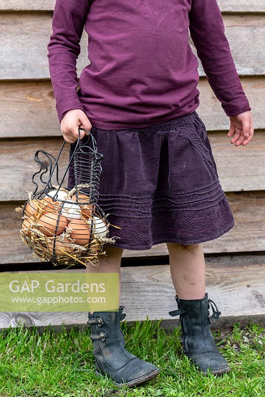 Fille portant un panier plein d'oeufs de poule dans un jardin