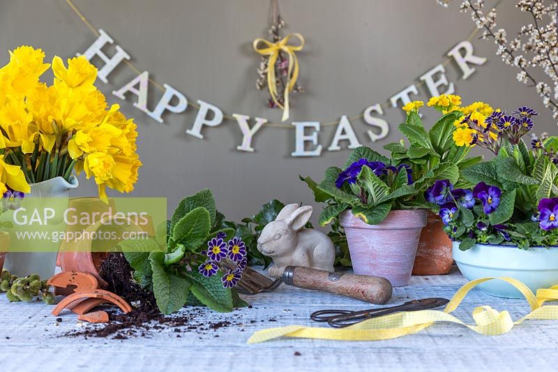 Arrangement de Pâques avec des fleurs de printemps, des outils, des pots, un lapin et un signe de Joyeuses Pâques