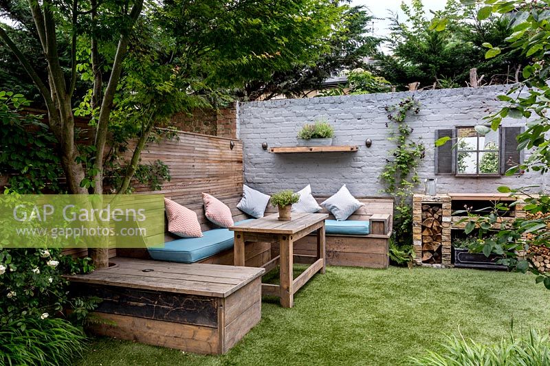 Petit jardin de la cour dans l'ouest de Londres avec pelouse artificielle, construit dans un coin salon et salle à manger avec échafaudage récupéré avec barbecue en brique Jardin conçu par James Walsh.