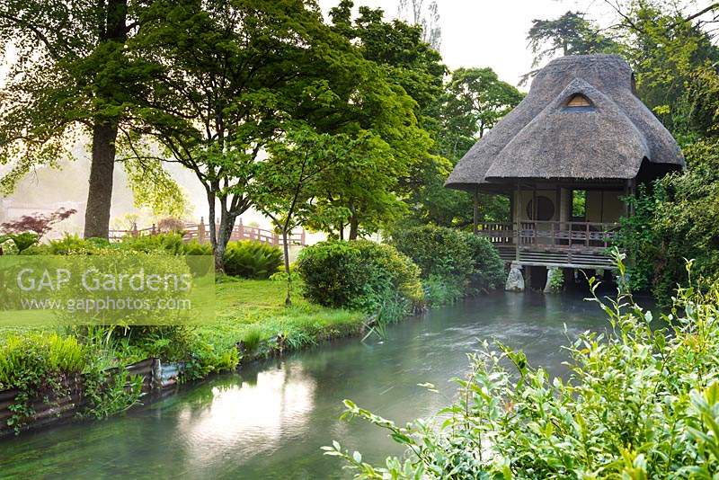 Maison de thé japonaise à cheval sur la rivière Avon qui traverse le jardin de Heale House, près de Salisbury, Wiltshire en mai avec le pont Nikkon rouge au-delà.