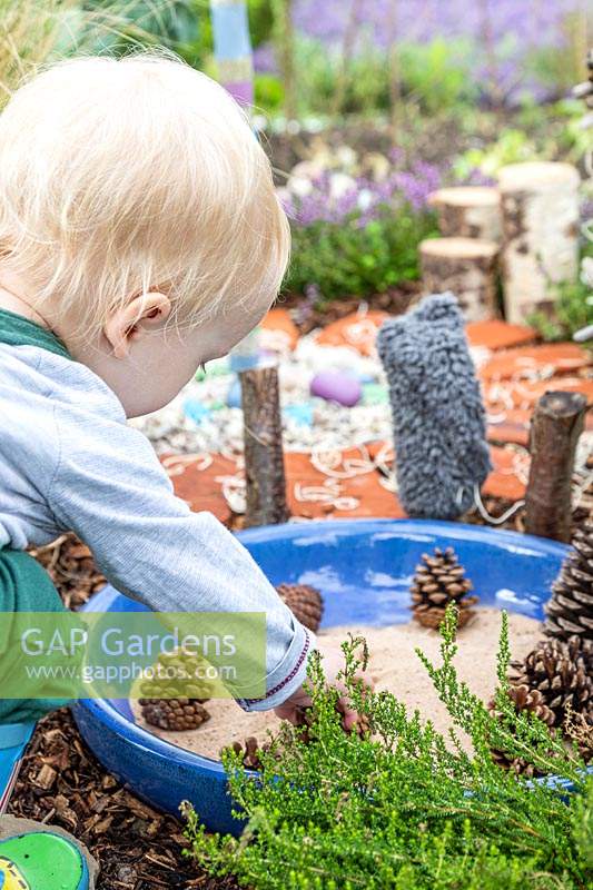 Jeune enfant jouant avec du sable et des pommes de pin dans le jardin sensoriel
