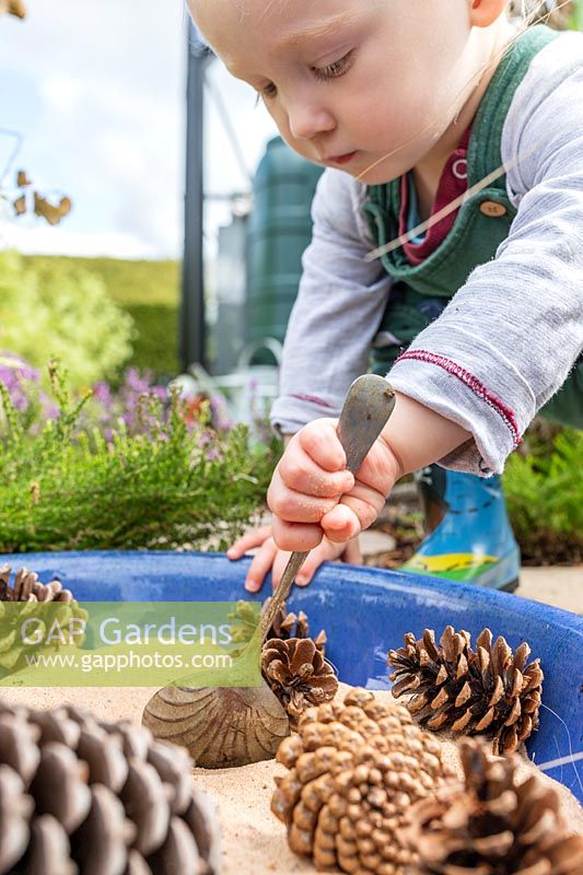 Jeune enfant jouant avec cuillère, sable et pommes de pin dans le jardin sensoriel