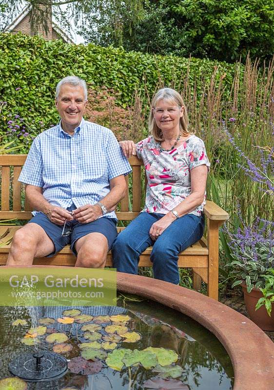 Les propriétaires de jardin se sont assis sur un banc par une pièce d'eau en acier corten