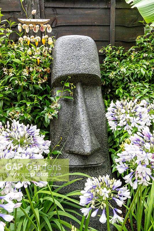 Sculpture inspirée de la tête de l'île de Pâques avec des agapanthes en premier plan