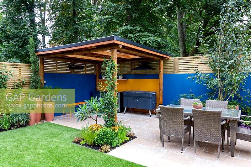 Patio et salle à manger extérieure avec barbecue couvert, entourés d'une clôture à lattes de bois contemporaine et d'un mur peint en bleu