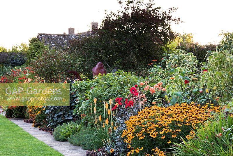 Le parterre de fleurs chaud à Bourton House, Moreton-in-Marsh en août, y compris Helenium 'Sahin's Early Flowerer', Dahlia 'Bishop of Llandaff', Kniphofia 'Mango Popsical' et des lys tigres.