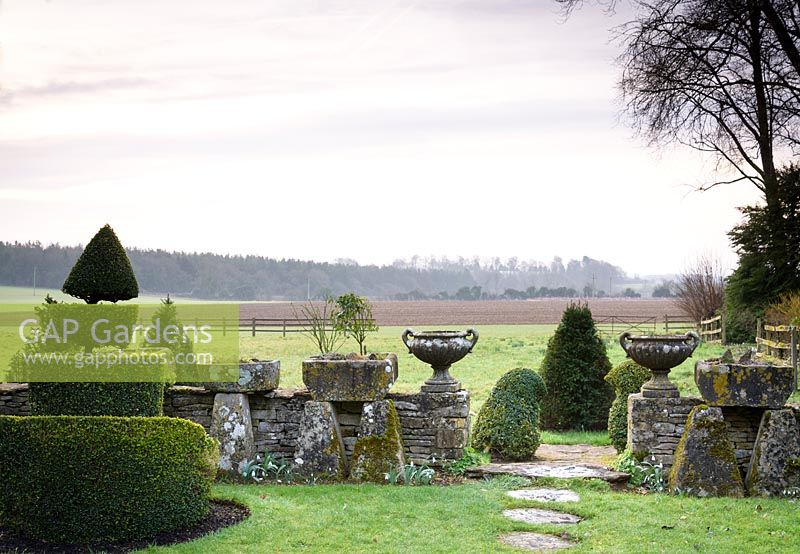 Paire d'urnes classiques affichées sur mur de pierre dans le jardin topiaire, avec vue sur les champs environnants à Rodmarton Manor, Glos, Royaume-Uni.