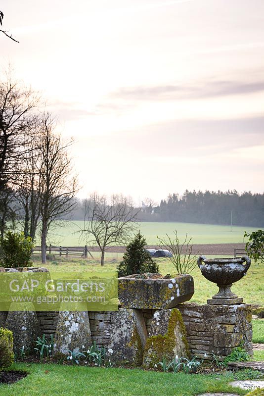 Mur de pierre bas affiché avec auges et urnes classiques, avec vue sur la campagne au-delà à Rodmarton Manor, Glos, UK.