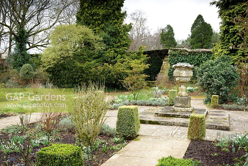 Le jardin de loisirs avec une urne en pierre et boîte taillée panachée en son centre à Rodmarton Manor, Glos, Royaume-Uni.
