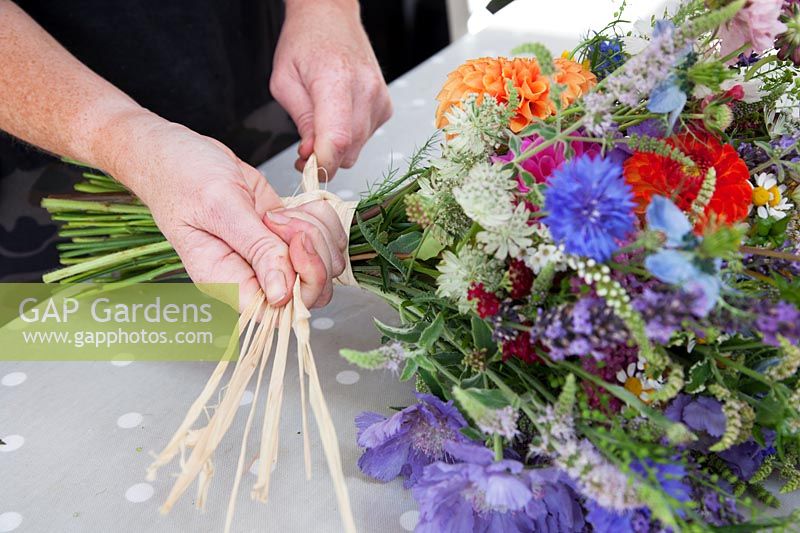 Zelie dans l'atelier de fleurs fabriquant des bouquets de fleurs attachés à la main et les fixant avec du raphia.
