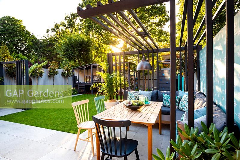 Vue sur salle à manger avec chaises colorées et pergola de style industriel au coucher du soleil.