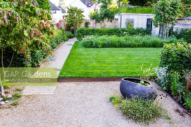 Un jardin de ville contemporain avec terrasse gravillonnée, bassin sculptural, pelouse surélevée, parterre de fleurs sauvages et jardin au toit vert.