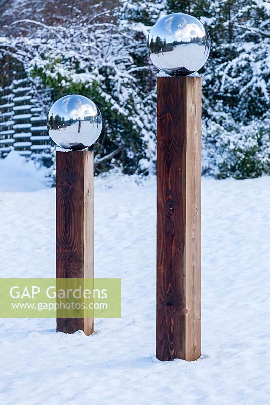 Paire de poteaux en bois surmontés de globes en acier inoxydable dans la neige. Jardin de la maison Veddw