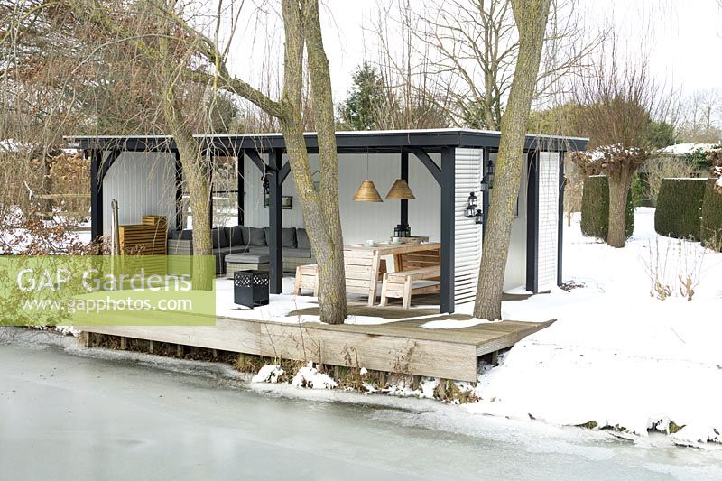 Maison d'été avec des meubles de salon confortables près du lac gelé au milieu d'un sol enneigé