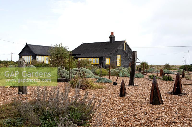 Cottage et jardin sur une plage de galets avec des objets trouvés et des plantes