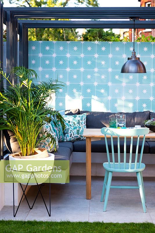 Salle à manger avec mur coloré, chaises, pergola moderne, lampe de style industriel et palmier dans le pot blanc.