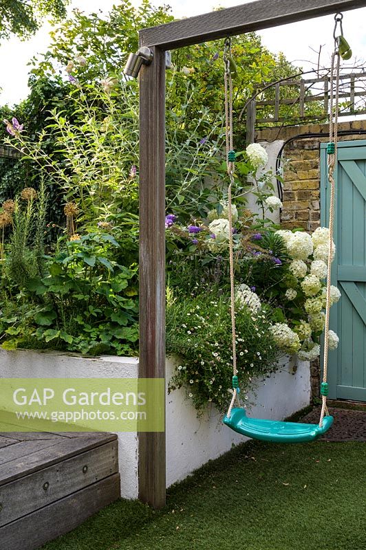 Family Small Hackney Garden - balançoire et parterre de fleurs surélevé avec plantation d'allium, d'hortensia blanc et d'Erigeronby Earth Designs