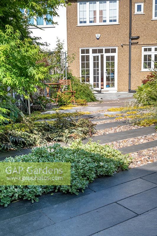 Vue sur zone pavée dans le jardin moderne du nord de Londres, avec pavage de schiste Ebony Cloud avec galets polis japonais.