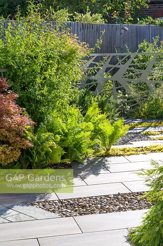 Jardin moderne dans le nord de Londres par Earth Designs, avec pavage de schiste Ebony Cloud, galets polis japonais et plantation d'aciers, de fougères et d'arbustes.
