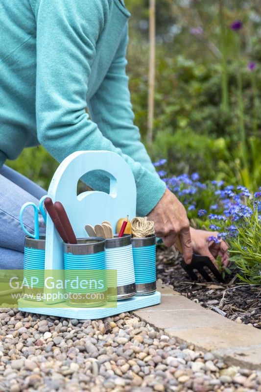 Boîte de conserve pastel sur le sol contenant des outils et des fournitures de jardinage avec une femme jardinant en arrière-plan