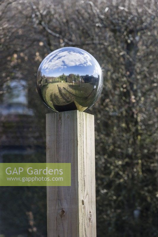 Globe en acier inoxydable reflétant le jardin environnant. monté sur colonne en bois. Février. Printemps