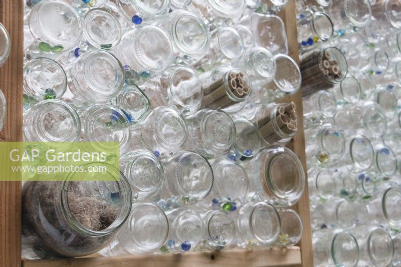 Les matériaux de nidification pour les oiseaux sont nichés dans des bocaux en verre tournés vers l'extérieur dans des murs de serre recyclés