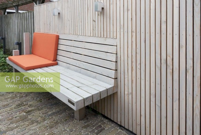 Banc en bois spécialement conçu à la clôture en bois avec coussins orange. Éclairage à la clôture.