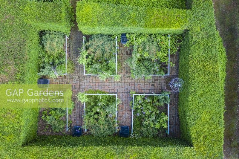 Vue sur petit jardin formel contenu par des haies d'ifs taillés ; image prise avec un drone. Allées de briques et parterres rectangulaires contenus par des garde-corps Juillet. L'été.