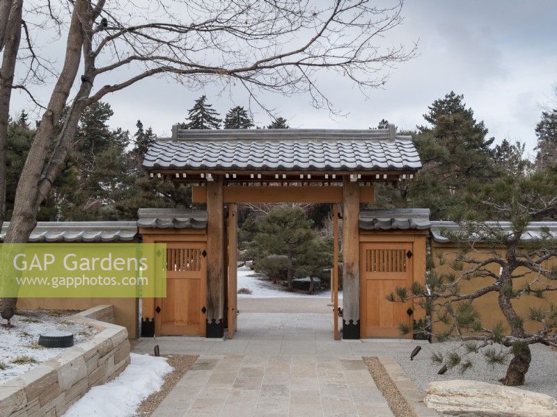 Photo d'hiver de l'entrée d'un jardin japonais avec des portes traditionnelles de style pergola. Mur de pierre, rochers et pin sculptural en premier plan