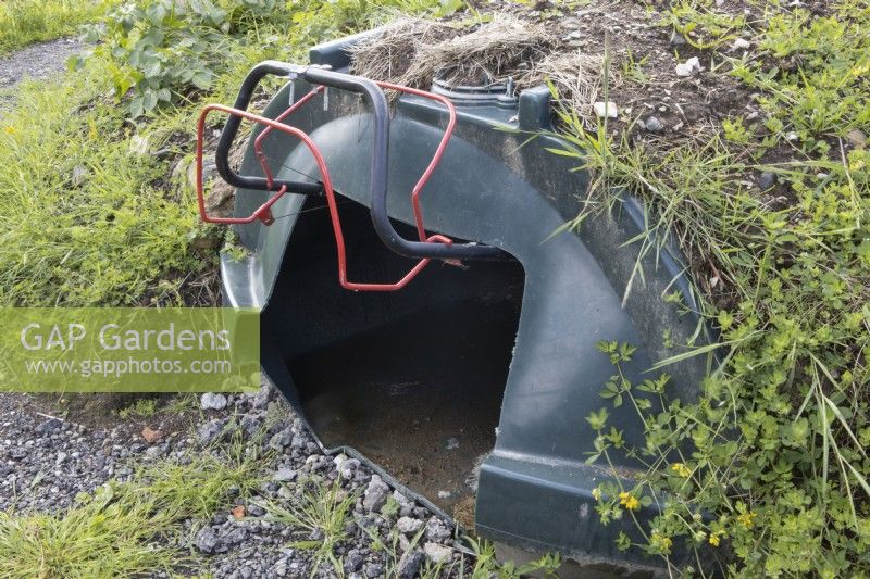 An old oil tank has been repurposed to make a home for a lawnmower. The tank has been dug into the bank beneath the lawned area of the garden. Derrydown. July. Summer. 