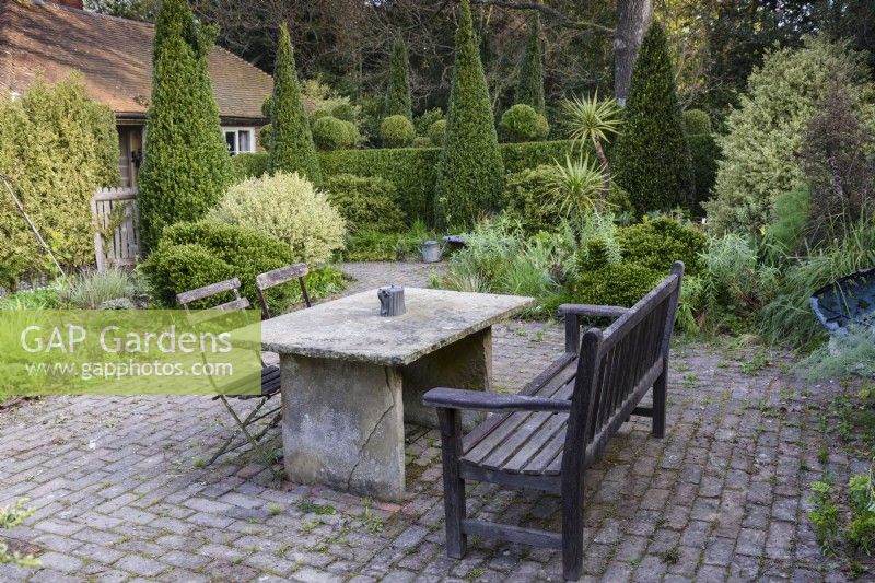 Table en pierre sur dallage en brique à Balmoral Cottage, Kent en avril entouré de conifères.
