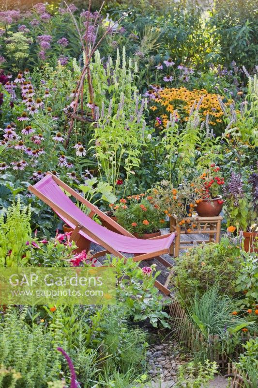 Transat sur petit patio parmi parterre de fleurs et pots mixtes colorés.