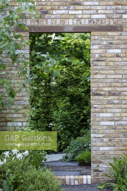 Mur de briques simple avec ouverture et vue à travers les parterres de jardin cultivés